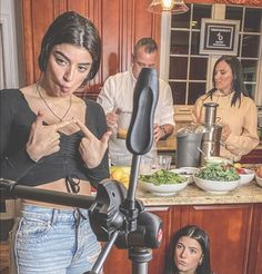 a woman standing in front of a camera next to two other people and bowls of food