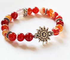 SUNFIRE Bracelet by Evil Queen Jewelry Natural Banded Agate in Sunset Fire Colors, Red Orange, a yellow and White Antique Silver Sun is the focal with antique Silver Accent Beads. Polished, Smooth, Natural Stone Stretch Bracelet measuring approximately 7 inches with 8mm round stones If you need a different length, please contact me! Each Stone is Unique and made by nature, no two are alike As with all jewelry, wear with care. Stones and metal do not always do well with chemicals or water. Best t Cheap Red Bracelets With Colorful Beads, Red Carnelian Beaded Bracelets, Adjustable Red Agate Crystal Bracelet, Red Crystal Bracelet With Natural Stones, Red Natural Stones Crystal Bracelet, Red Agate Gemstone Beaded Bracelets, Handmade Red Agate Bracelets, Orange Beaded Bracelets, Fire Bracelet