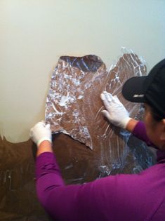 a woman in purple shirt and white gloves working on a piece of tin foil covered wall