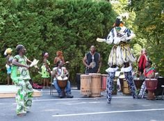 some people are standing in the street with drums and drum sets on their feet while others watch