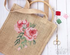 a cross stitch bag with flowers on it next to scissors and thread