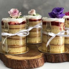 four small cakes with forks and flowers in them sitting on a wooden slice that is tied to a piece of wood