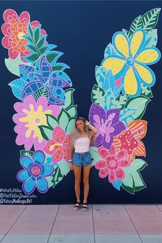 a woman standing in front of a wall with flowers painted on it