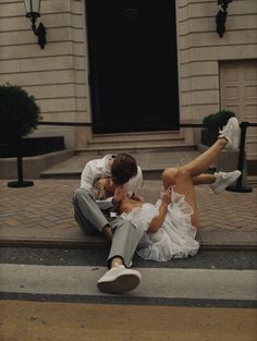 a man and woman sitting on the ground in front of a building with their legs crossed