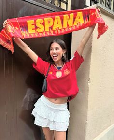 a woman holding up a red scarf in front of a doorway with spanish writing on it