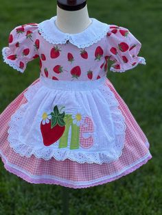 a pink and white dress with strawberrys on it is sitting on a mannequin