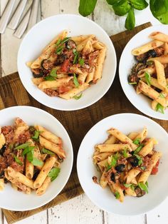 four white bowls filled with pasta and meat on top of a wooden cutting board next to silverware