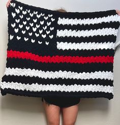 a woman is holding up a crocheted american flag pillow with hearts on it