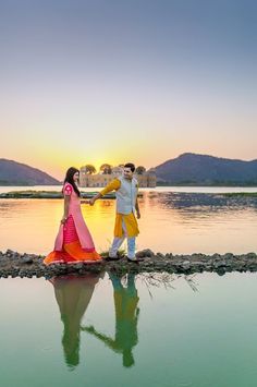 a man and woman standing on the edge of a body of water with their arms around each other