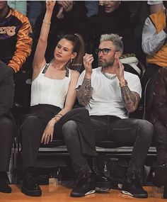 a man and woman sitting next to each other in front of a crowd at a basketball game