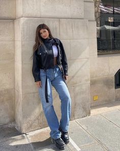 a woman leaning against a wall wearing jeans and a leather jacket