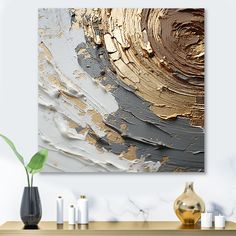 an abstract painting in gold and silver on a white wall above a table with vases