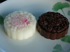 two chocolates on a plate with green leaves around them and one has a pink frosting in the middle