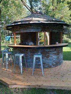 an outdoor bar with stools on a wooden platform in the middle of a park