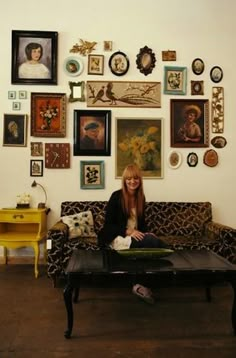 a woman sitting on top of a couch in front of a wall full of pictures