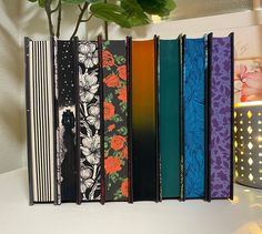 an assortment of books are lined up on a shelf next to a potted plant