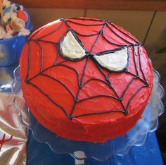 a spiderman cake is sitting on a plastic table with other desserts in the background