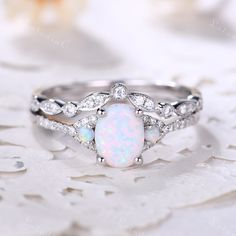 a white opal and diamond ring sitting on top of a lace covered tablecloth