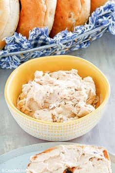 a bowl of cream cheese next to a loaf of baguette bread on a table