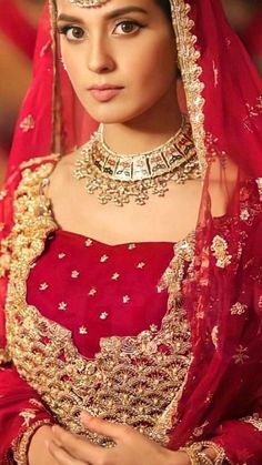 a woman wearing a red and gold bridal outfit with her hands on her chest