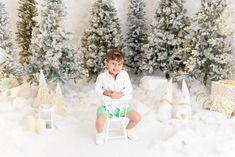 a little boy sitting on a chair in front of christmas trees