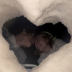 a man and woman are looking into a heart - shaped hole in the snow