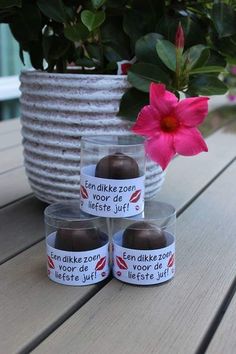 three plastic containers with chocolates in them on a table next to a pink flower