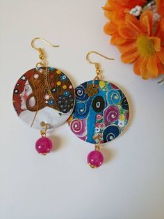 two colorful earrings are sitting on a table next to an orange flower and a vase with flowers in it