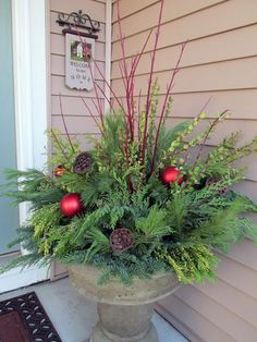 a potted plant with pine cones and evergreen branches on the front porch for christmas