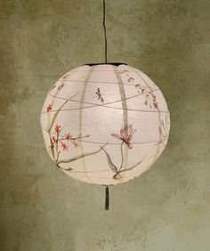 a white paper lantern hanging from a wire with flowers on it and two birds perched on the branch