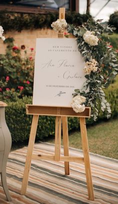 an easel with flowers and greenery on it sitting in front of a sign