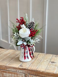 a white vase filled with flowers and greenery on top of a wooden table next to a pine cone