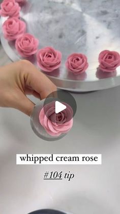 someone is decorating pink roses with icing on a silver cake platter that reads whipped cream rose