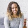 a woman sitting at a table with some food and drinks in front of her smiling