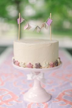 a white cake sitting on top of a table covered in pink and purple decorations with flags