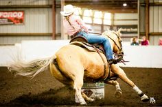 a woman riding on the back of a brown horse in an indoor arena with people watching