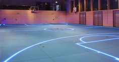 an indoor basketball court is lit up with blue lights and white lines on the floor