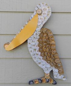 a bird made out of bottle caps on the side of a building with a yellow beak