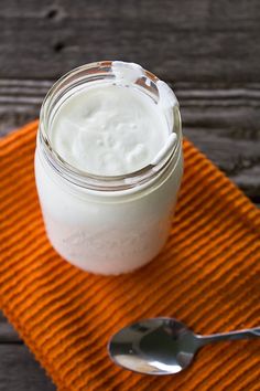 a glass jar filled with yogurt sitting on top of an orange towel next to a spoon