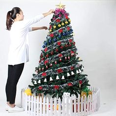 a woman is decorating a christmas tree in front of a white picketed fence