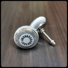 two white and gold ceramic knobs sitting on top of a wooden table next to a screw