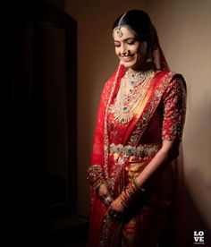 a woman in a red and gold bridal outfit smiling at the camera with her hands on her hips