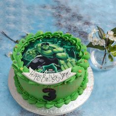 there is a green cake with the hulk logo on it next to a flower vase