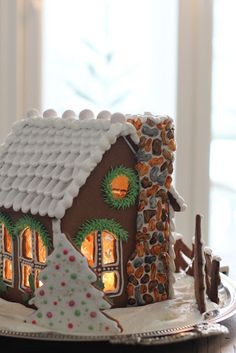 a gingerbread house decorated with icing and decorations on a platter in front of a window