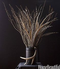 a vase filled with dried plants on top of a black table next to a wall