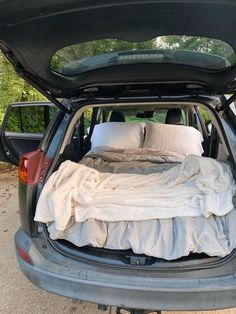 the back end of a car with an open trunk filled with blankets and two pillows