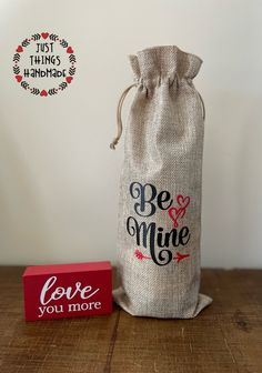 a bag with the words be mine on it next to a small red box that says love you more