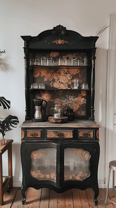 an old fashioned black china cabinet with glassware on the top and bottom shelf, in front of a white wall