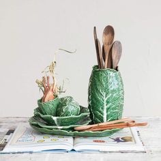 a book and some wooden spoons in a green vase on top of a table