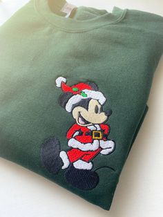 a green mickey mouse christmas sweatshirt with santa clause on it's chest and ears